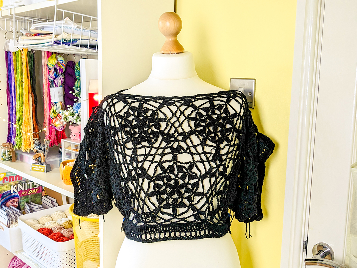 A crocheted lace crop top in all black, made from repeating hexagonal lace motifs joined together.