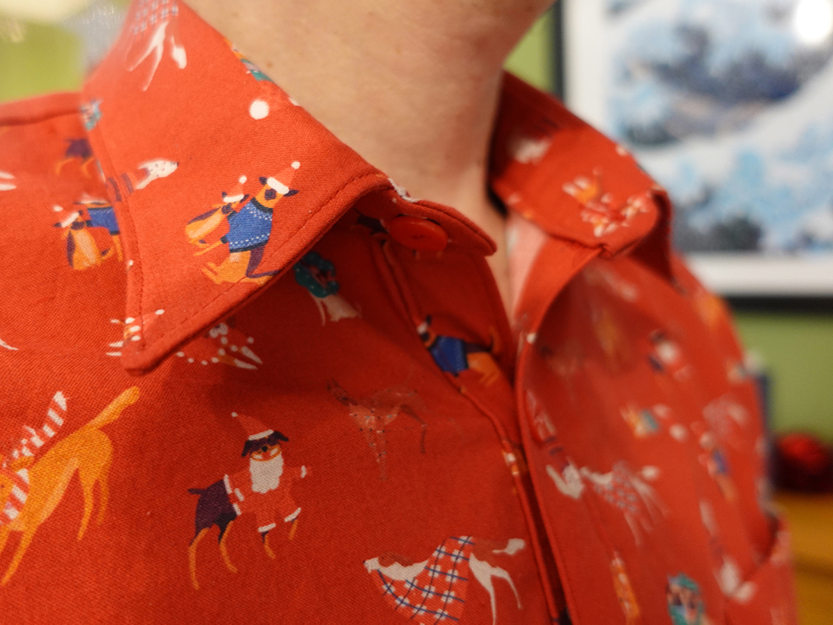 Closeup on the collar of a home sewn shirt, made of red fabric with a pattern of Christmassy dogs.